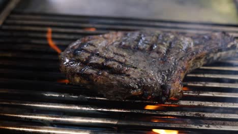 chef flipping cooked steak on a grill with high flame