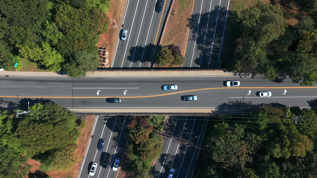 An aerial, top down view of an overpass which crosses the Southern State Parkway on Long Island, NY in the day. Traffic travels in all directions as the camera is tilted downwards