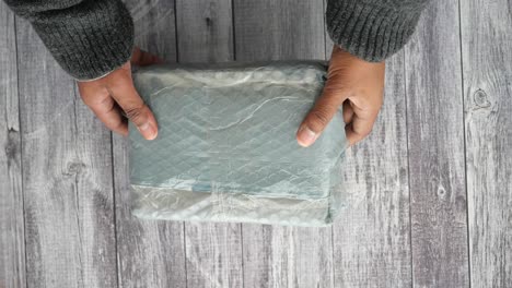 hands holding a wrapped package on a wooden table