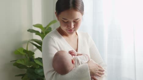 young asian mother holding and lulling her newborn baby in bedroom