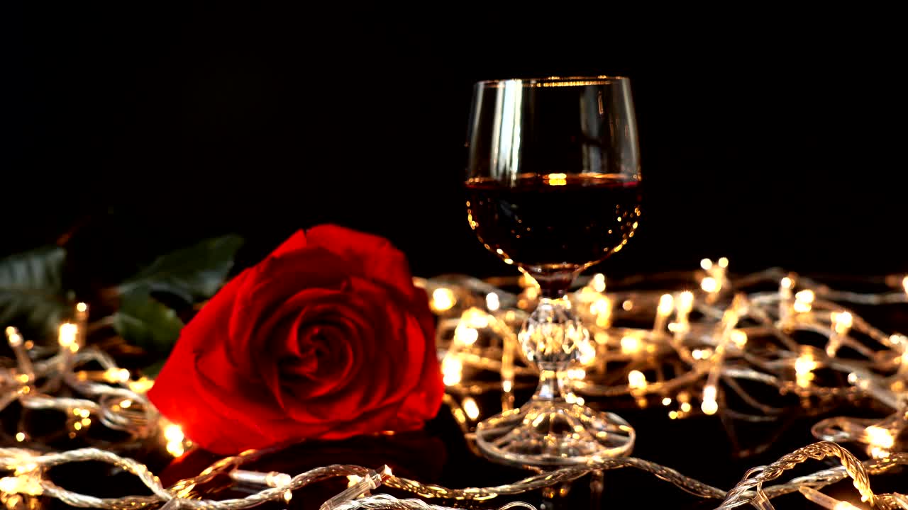 Copa de vino y una rosa sobre un fondo de guirnaldas luminosas.