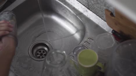 persona lavando vidrio con agua y jabón para lavar platos en el fregadero de la cocina - toma en ángulo alto
