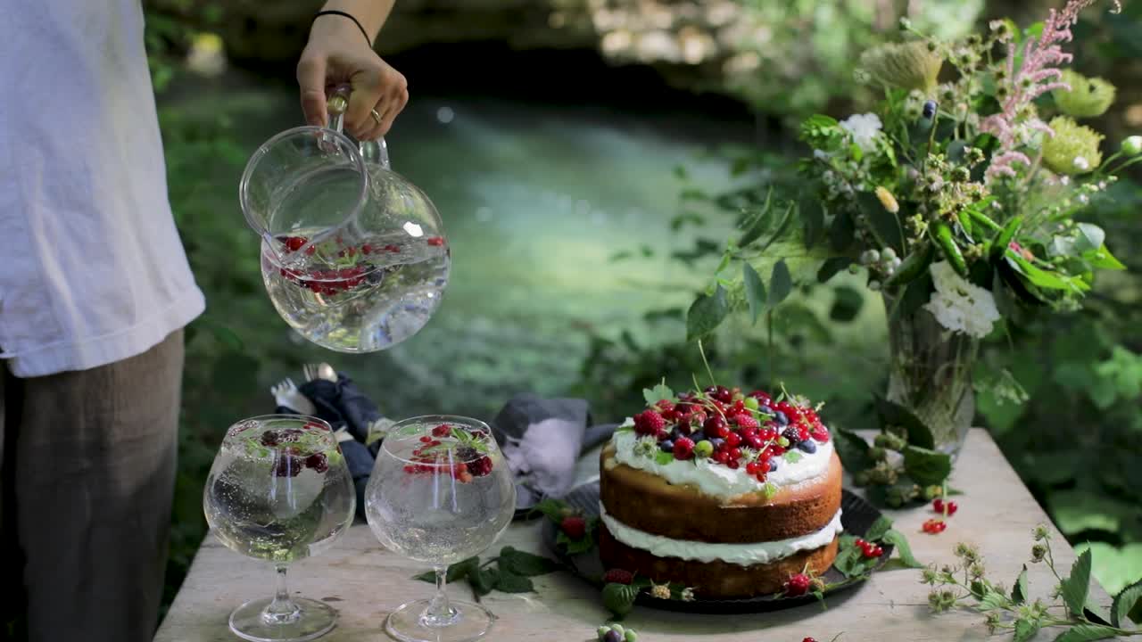Nærbillede af en tjener, der hælder forfriskende bær-vand i glas ved en havefest med gourmetkage