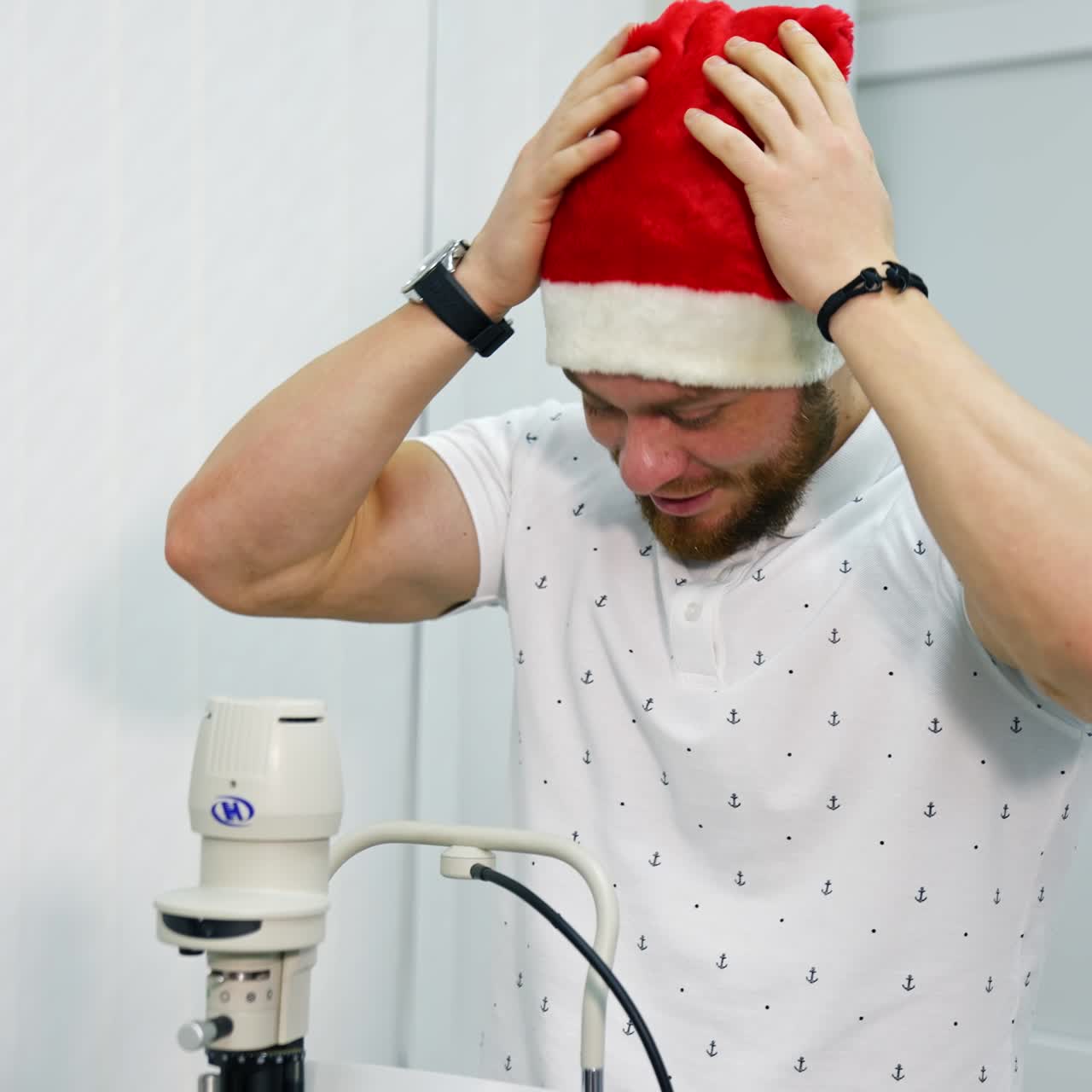 Man putting on Christmas cap in clinic. Smiling man visits ophthalmologist at Christmas. Male patient consulting at oculist