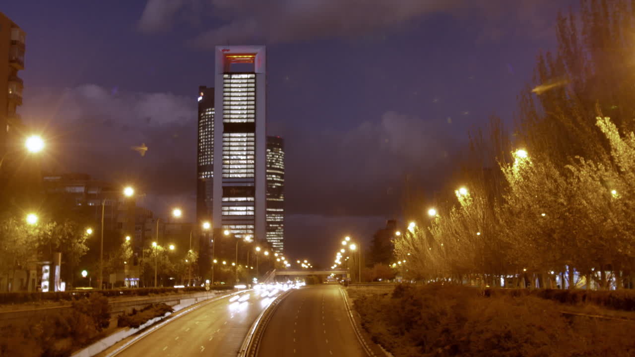 escena nocturna dinámica en una ciudad madrid con rascacielos iluminados en colores vibrantes y semáforos que atraviesan la calle