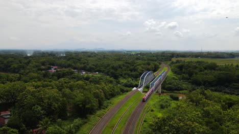 Aerial-follow-shot-of-train-crossing-river-bridge-in-rural-area-of-Indonesia-during-cloudy-day