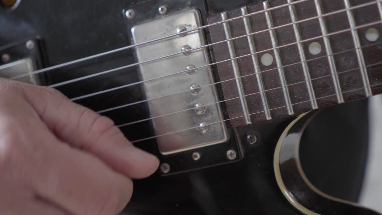 A close-up image of a guitarist's right hand picking the strings on a black 335 style electric guitar