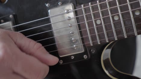 A close-up image of a guitarist&#039;s right hand picking the strings on a black 335 style electric guitar
