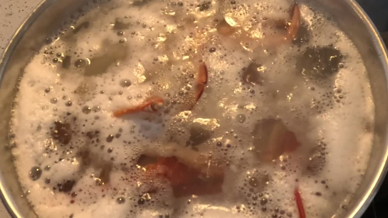 Close-up of vegetables boiling in a frothy broth on a stovetop, with a lid being lifted.