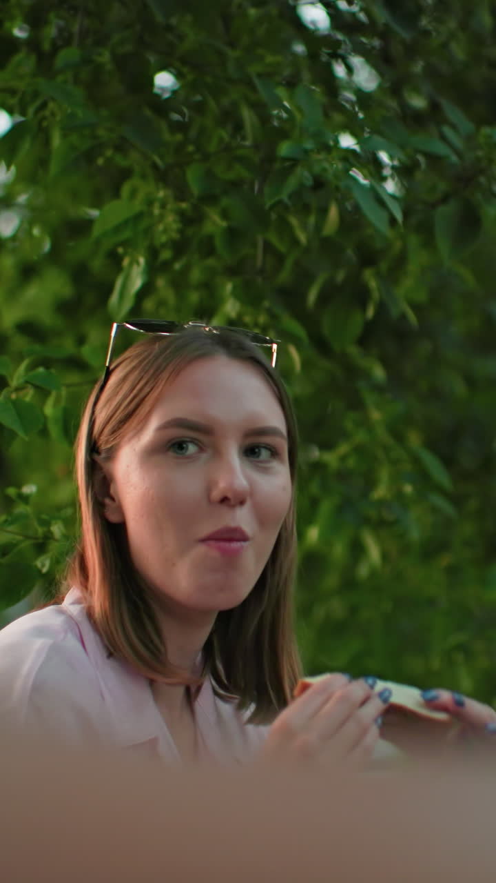 을 들고 토스트를 하는 문신한 손으로 미소 짓는 남자의 클로즈업, 배경에 을 고 있는 여성, 나무를 통해 필터링되는 빛