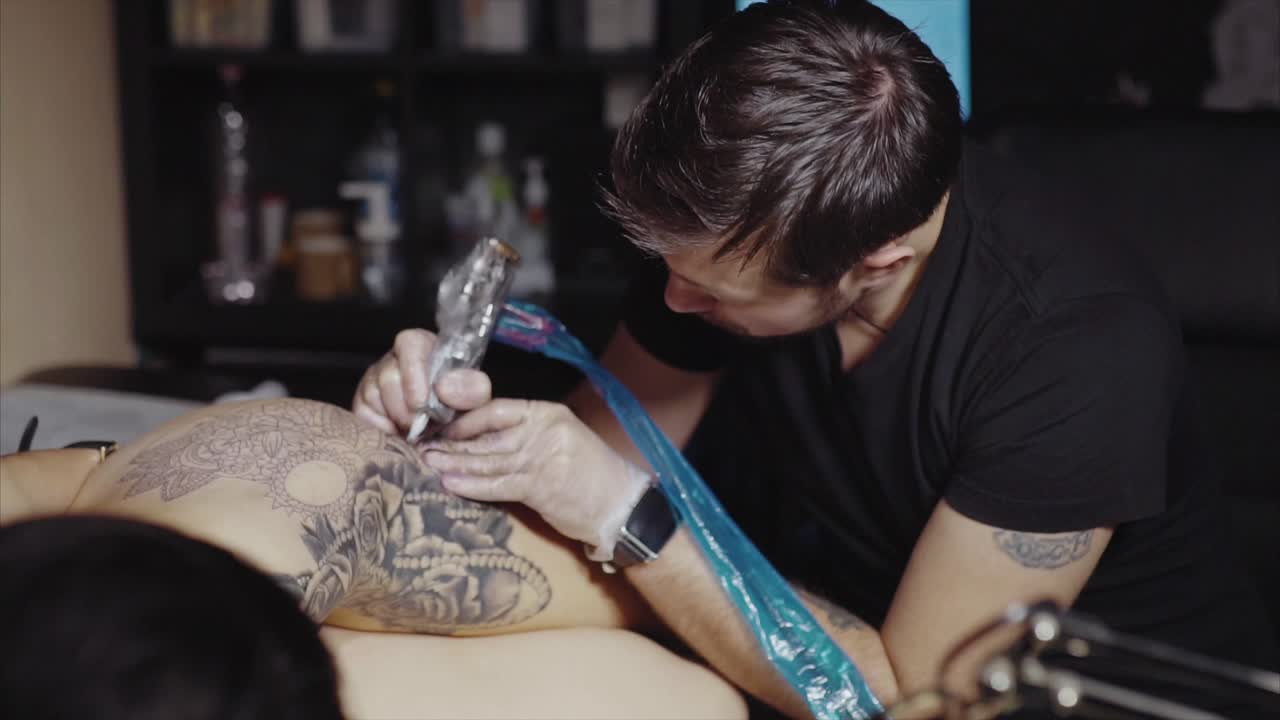 Tattoo artist working on a detailed tattoo design on a woman's back