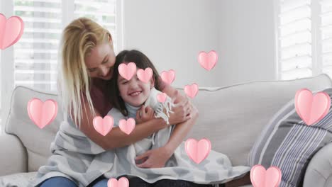 Animation-of-hearts-over-happy-caucasian-woman-and-her-daughter-sitting-on-sofa,-embracing