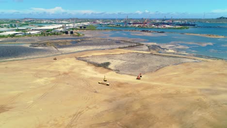 aerial drone dolly tilt down to excavator and loader in sandy asphalt lake cleanup pit in curacao