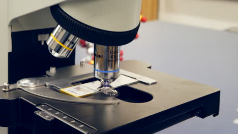 Close-up-on-microscope-lenses-and-a-slide-with-human-cancer-cells-in-a-science-and-medical-research-lab-classroom