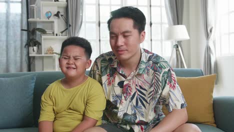 child cry while sitting with his father on a couch and watching tv at home, spending time together at home