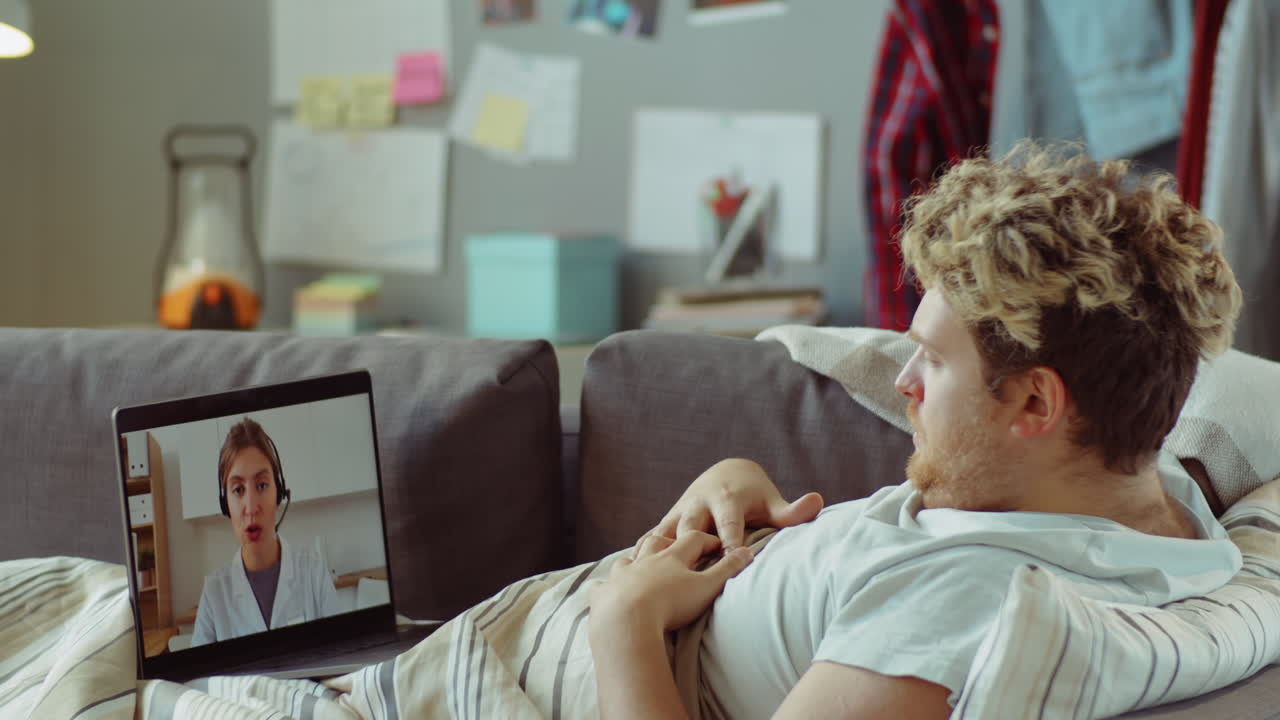 Sick Man Lying on Sofa and Speaking with Doctor on Video Call