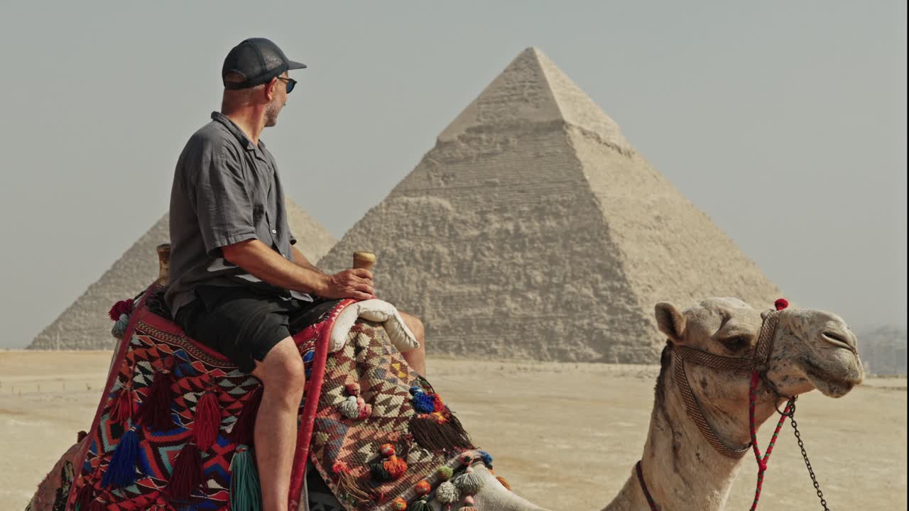 Esperienza di viaggio egiziana classica: un uomo seduto in cima a un cammello sull'altopiano di Giza. Il cammello è adornato con una sella vivace e dai motivi tradizionali.