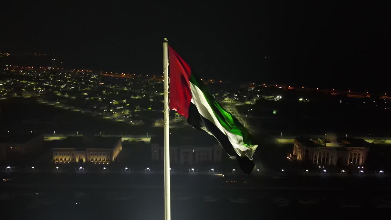 4k: vista aérea nocturna de la bandera de los emiratos árabes unidos ondeando en el aire, el símbolo nacional de los emiratos árabes unidos-1