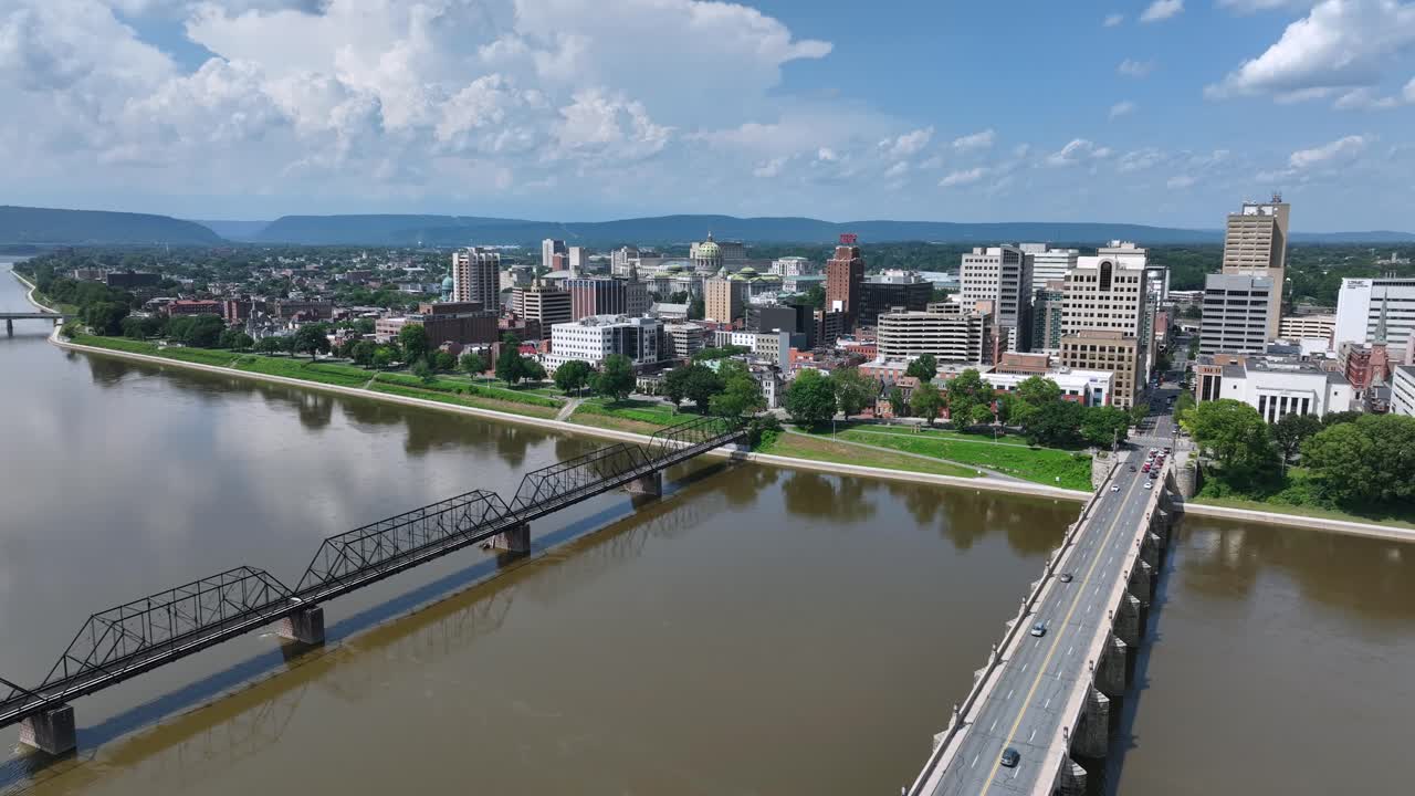 Paesaggio urbano di Harrisburg con acqua di fiume marrone sporca in America. Giornata di sole in Pennsylvania. Ponte per auto e ponte ferroviario. Ampia ripresa aerea all'indietro.