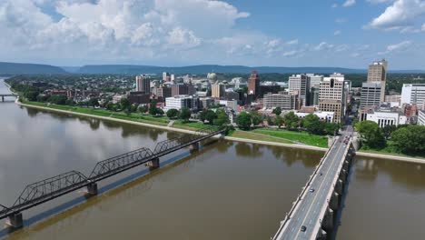 cityscape of harrisburg with dirty brown river water in america. sunny day in pennsylvania. bridge for cars and railway track bridge. aerial backwards wide shot