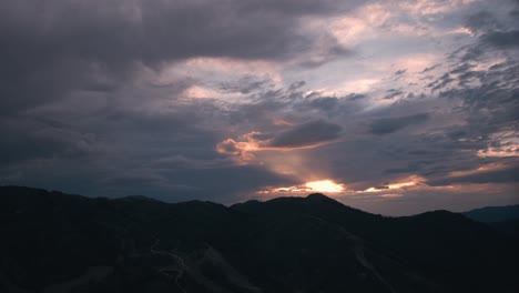 aerial hyperlapse of sun setting behind clouds and mountains as dark stormy clouds roll in