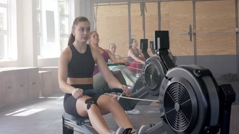 focused unaltered diverse women exercising on rowing machines at gym, in slow motion