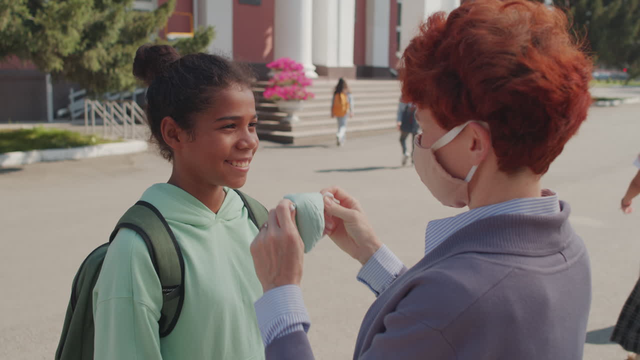 Caring Woman Putting Face Mask on Schoolgirl