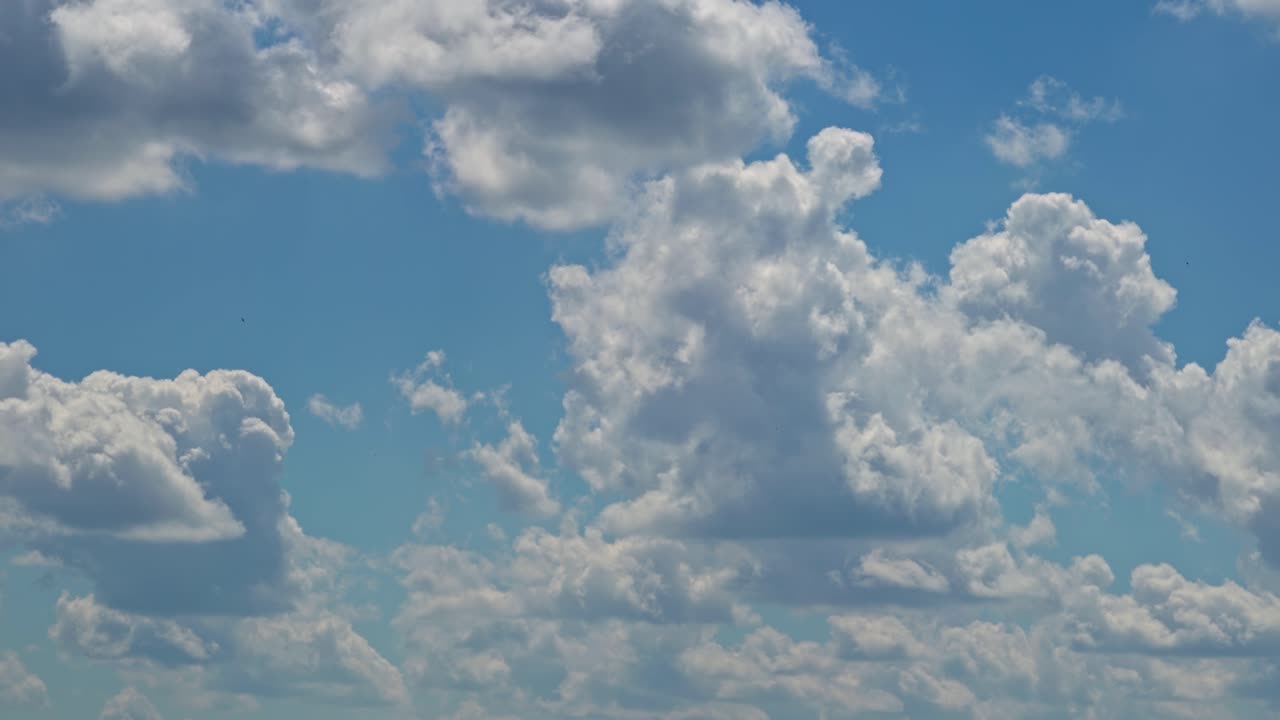 Fluffy clouds gather in the blue sky over an open landscape during midday