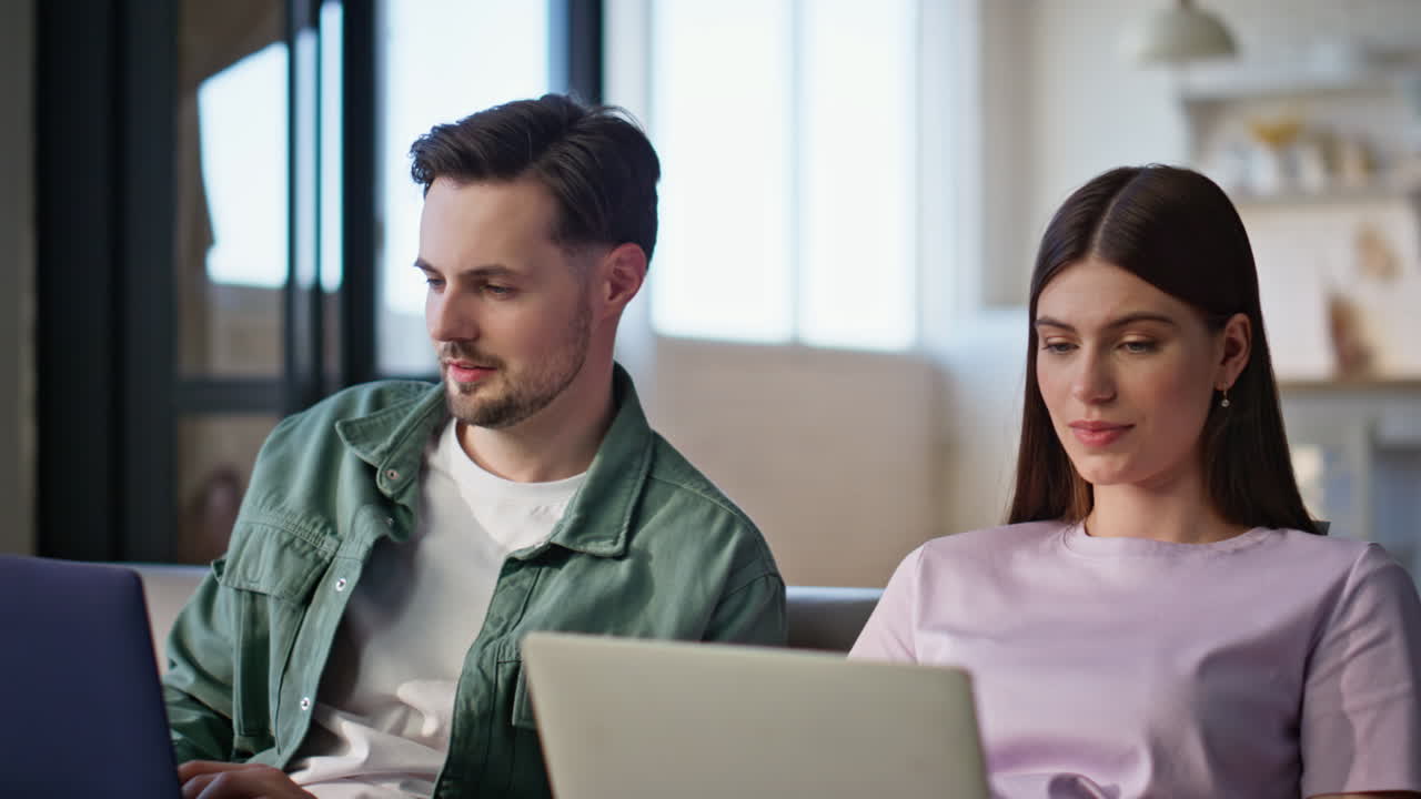 Closeup colleagues working laptops at living room interior. Talking pair work