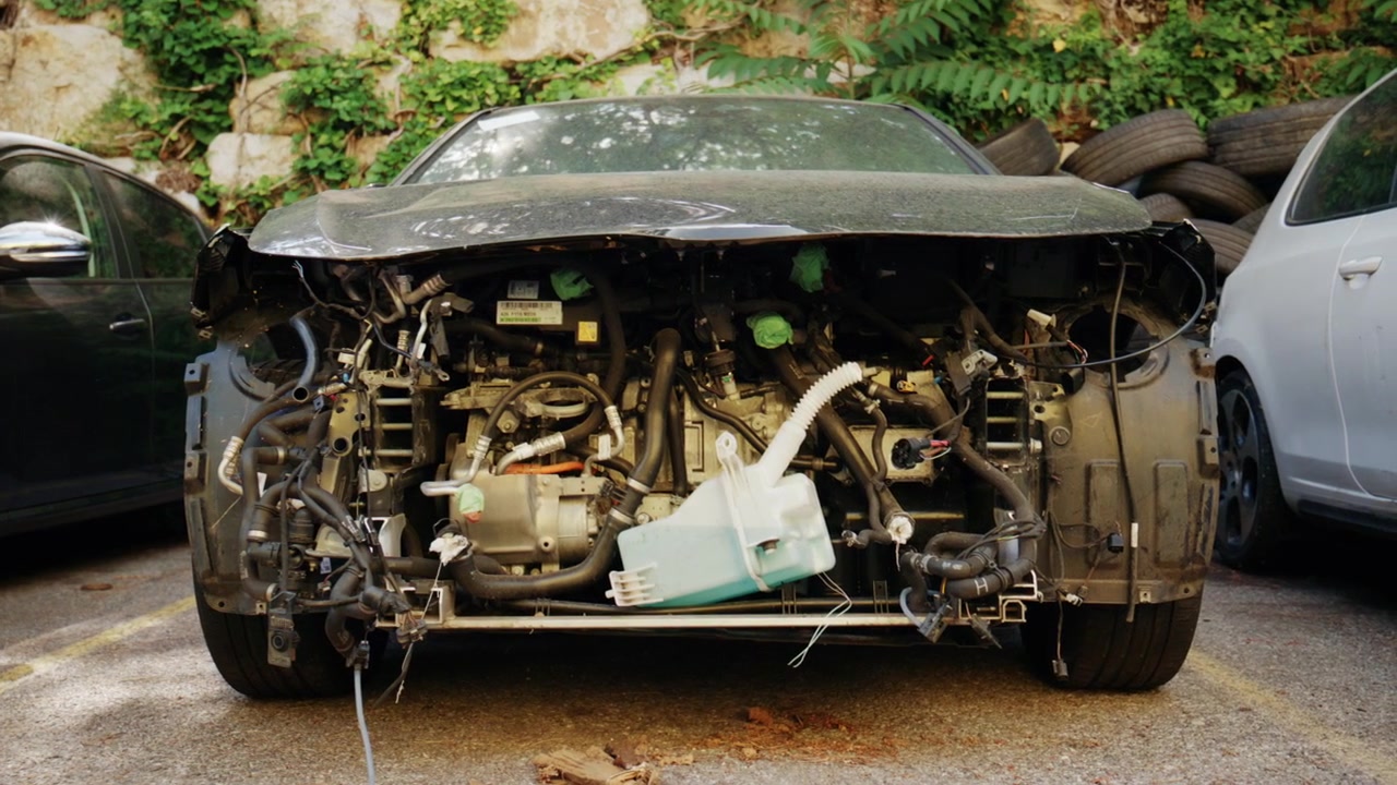 Close up front view of a dismantled car with exposed engine components, hoses, wiring, and missing body panels
