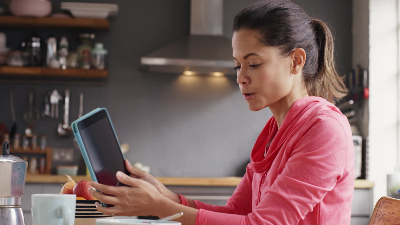 hermosa mujer de raza mixta hablando con un amigo tomando el desayuno en casa usando una aplicación de tableta digital