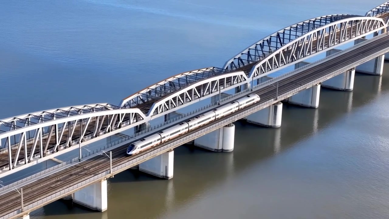 Sleek white high speed train gliding across curved steel arch bridge above calm river, seen from elevated aerial viewpoint with clear blue sky, strong symmetry, and modern transport engineering