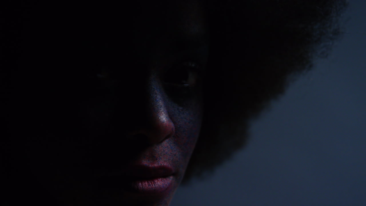 retrato de cerca de una hermosa mujer afroamericana que usa pintura exótica para la cara arte corporal mujer misteriosa con maquillaje colorido luz parpadeante en fondo oscuro concepto de expresión creativa