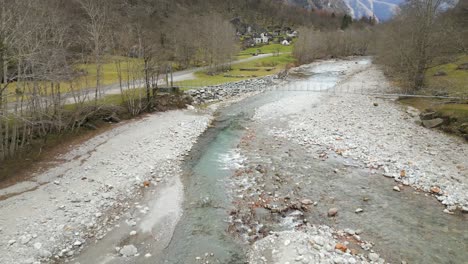 in peaceful countryside where a shallow river runs on the rocky riverbed, trees are standing grey and naked, while fallen leaves are scattered here and there on the rocks and below the trees
