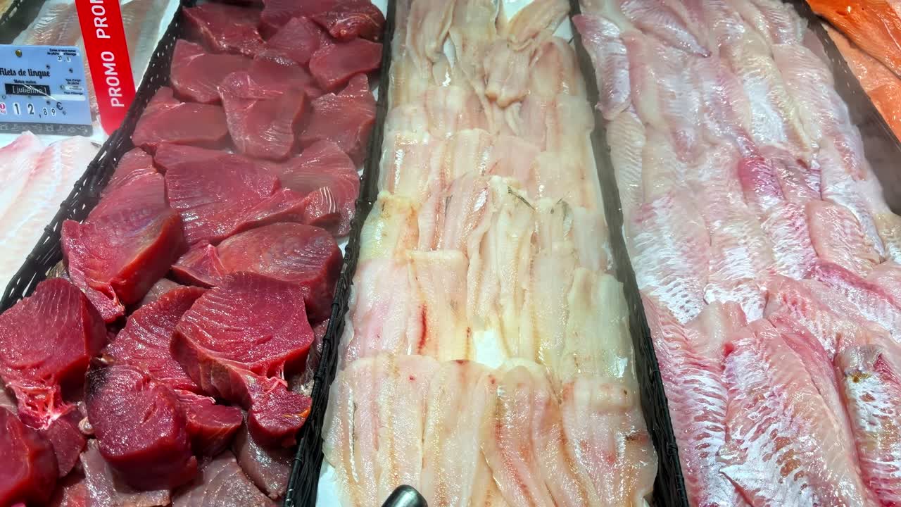 A variety of fresh fish fillets including tuna and salmon are neatly arranged in a seafood market display. Ideal for culinary content or seafood industry promotions