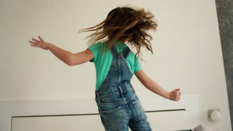 Happy-little-girl-dancing-while-listening-to-music-on-smartphone-with-headphones-in-living-room