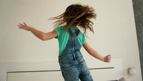 happy little girl dancing while listening to music on smartphone with headphones in living room