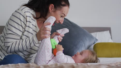 madre caucásica jugando con su bebé sosteniendo un juguete en la cama en casa