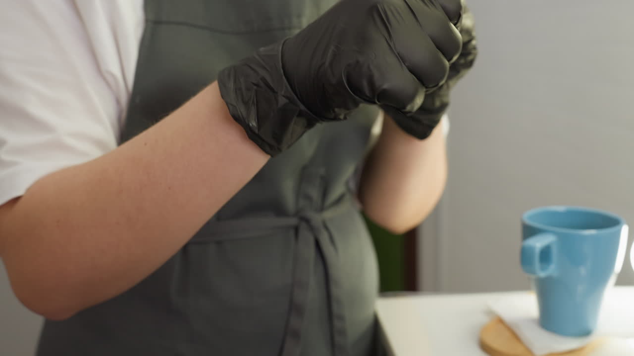 Beautician in black gloves applies small amount of cream to brush and cleans it using cotton pad while talking to client during eyebrow grooming session in well-lit professional beauty salon