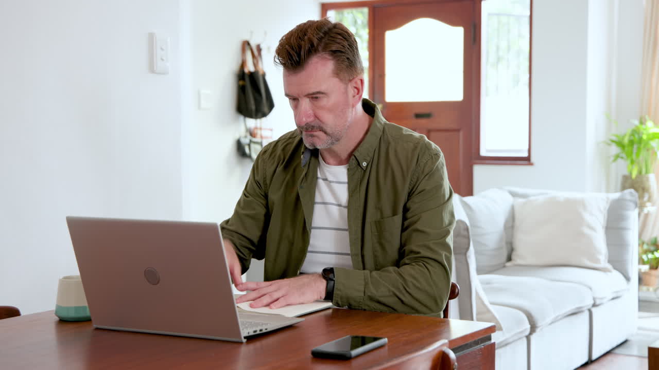 Senior man working on laptop at home, focused and engaged in task