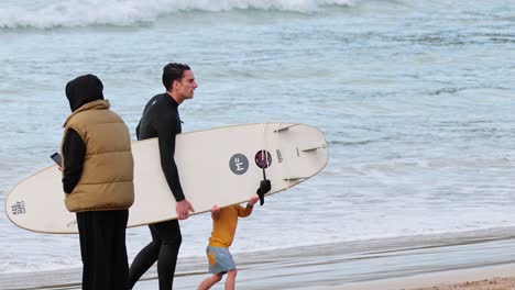 family walking with surfboard on the beach