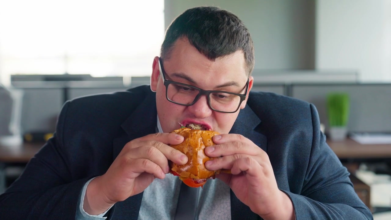 Uomo in abito che si gusta un grande hamburger in ufficio