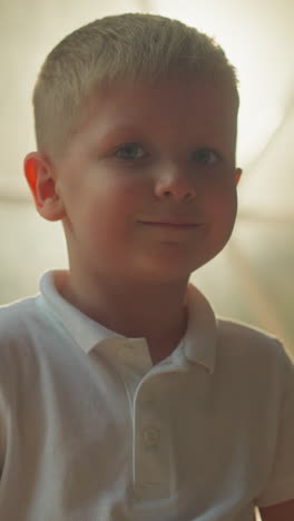 kid smiles and looks at camera standing in front of lighted transparent film of tent. cute blond preschooler enjoys evening outdoors at glamping site closeup on blurred background