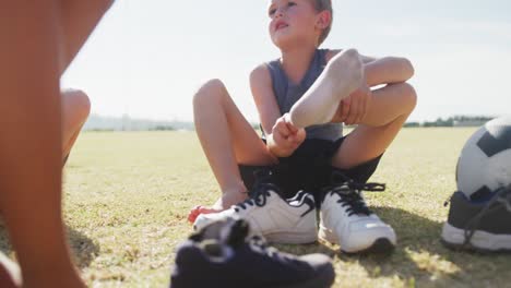 Video-Von-Glücklichen,-Vielfältigen-Jungen,-Die-Auf-Dem-Rasen-Sitzen-Und-Socken-Ausziehen