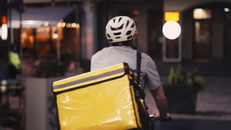 food delivery courier wearing thermal backpack rides a bike at night to deliver orders for clients and customers