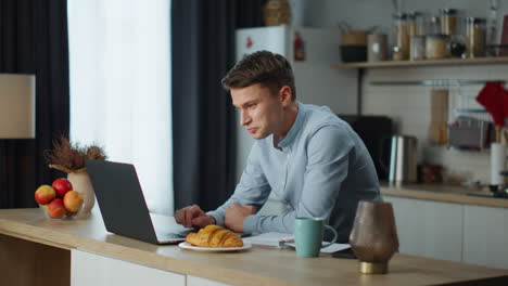 freelancer man satisfied work sitting at kitchen table with modern laptop.