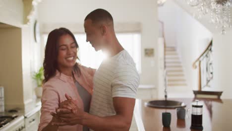 happy biracial couple dancing together in kitchen