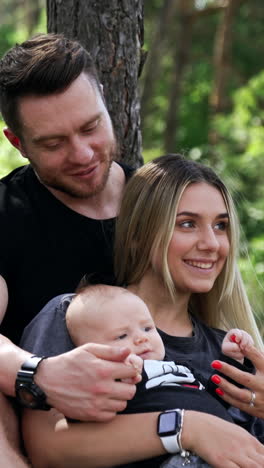 happy caucasian couple rest in the forest with their baby. smiling woman holding her child's tiny hand. vertical video