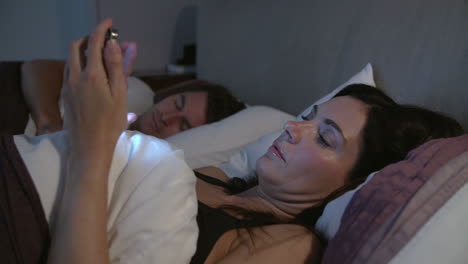 Mujer-Usando-Teléfono-Móvil-En-La-Cama-Mientras-Su-Pareja-Duerme