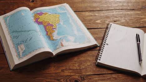 open book with map and notebook on wooden desk